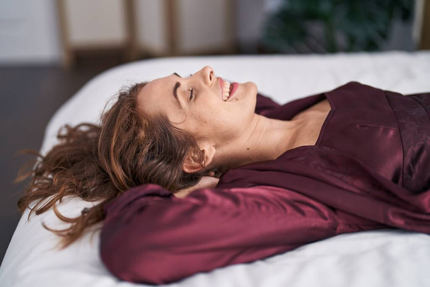 Молода жінка посміхається впевнено лежить на ліжку в спальні
 - Фото, зображення