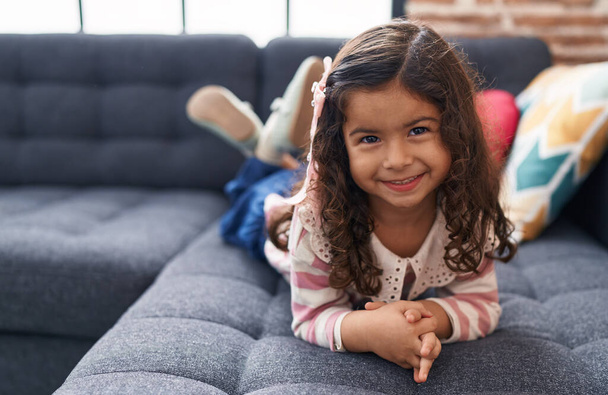 Rozkošná hispánská dívka se usmívá doma na pohovce - Fotografie, Obrázek