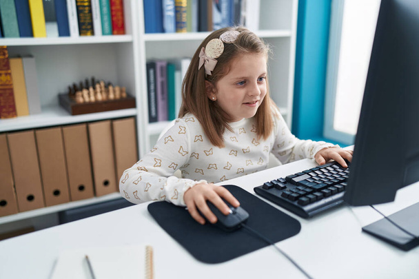 Adorable blonde girl student using computer sitting on table at classroom - Photo, Image