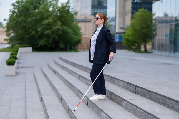 Blind business woman descending stairs with a tactile cane from a business center - Foto, afbeelding