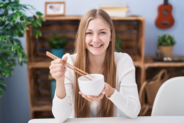 Young caucasian woman eating asian food using chopsticks winking looking at the camera with sexy expression, cheerful and happy face.  - Foto, Imagen