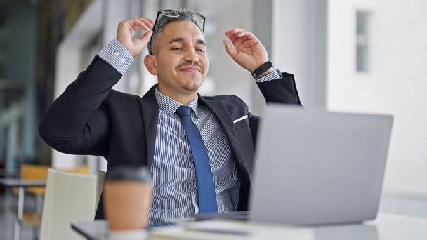 Genç İspanyol iş adamı ofiste dizüstü bilgisayar kullanıyor. Gözlüklerini çıkarıyor. - Fotoğraf, Görsel