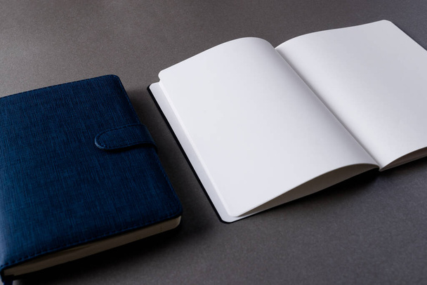 Close up of blue notebook and open book with copy space on grey background. Literature, reading, writing, leisure time and books. - Fotografie, Obrázek