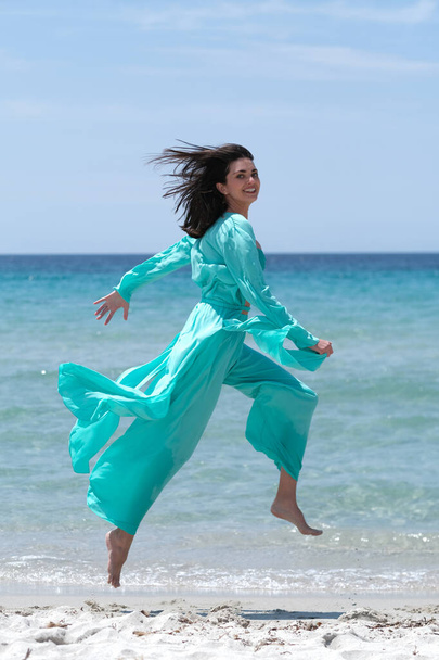 Beautiful brunette in turquoise clothes on the beach. - Zdjęcie, obraz