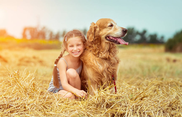 happy little girl with her dog golden retriever in rural areas in summer - Фото, изображение