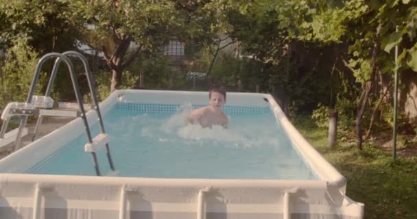 Ragazzo che si diverte in piscina nel cortile in estate, spruzzando acqua - Filmati, video