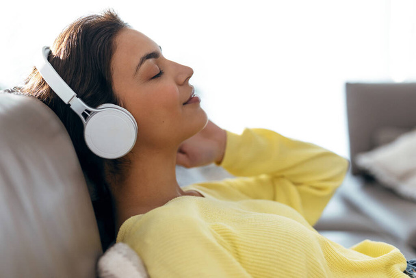 Shot of relaxed woman listening to music with smartphone while lying on sofa at home. - Foto, Imagem