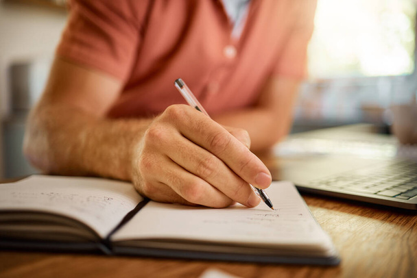 Man, hands and writing on book with pen for notes, schedule planning or strategy on table at home. Closeup hand of male person with notebook for ideas, reminder or information in research or studying. - Фото, изображение