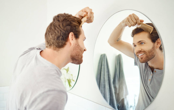 バスルームミラー、反射と成長維持、美容ルーチンや衛生クリーニング治療のための幸せな男のブラシ髪。笑顔、朝と豊かな健康的な髪型のための竹櫛を持つ家の人. - 写真・画像