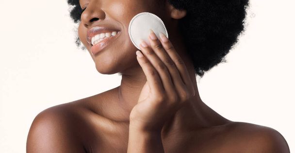 Black woman, beauty and cotton pad in hand with skincare and natural cosmetics on white background. Cleaning makeup from face, wellness and skin glow, African female model with smile and dermatology. - Фото, изображение