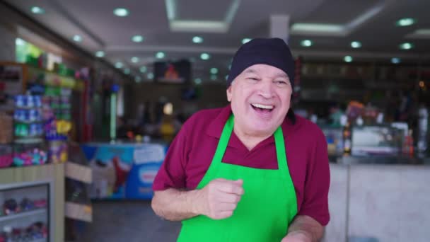 Un empleado mayor feliz de la cafetería bailando y celebrando grandes noticias. Emocionado Hombre mayor caucásico vistiendo uniforme, delantal y sombrero de pelo - Imágenes, Vídeo