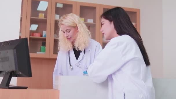 Deux membres du personnel médical professionnel, une femme asiatique médecin, et un pharmacien blanc ont discuté des prescriptions de médicaments de traitement au comptoir du département de pharmacie de la clinique hospitalière. - Séquence, vidéo