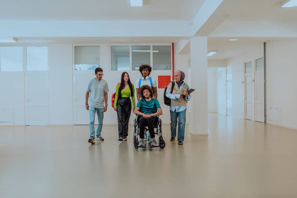 En una universidad moderna, un grupo diverso de estudiantes, incluyendo un estudiante afroamericano y una mujer que usa hiyab, caminan juntos en el pasillo, acompañados por su colega en silla de ruedas - Foto, imagen