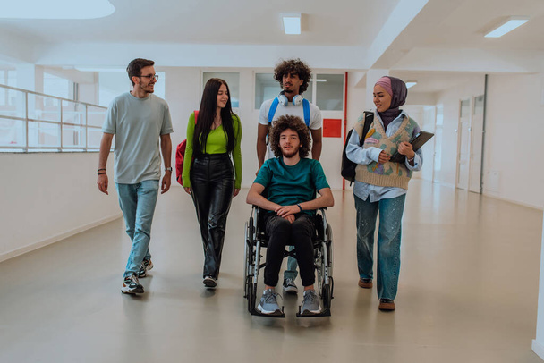 В современном университете разнообразная группа студентов, в том числе афроамериканская студентка и женщина в хиджабе, идут вместе по коридору в сопровождении своего коллеги по инвалидной коляске - Фото, изображение