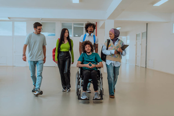 Σε ένα σύγχρονο πανεπιστήμιο, μια ποικιλόμορφη ομάδα φοιτητών, μεταξύ των οποίων μια Αφρο-Αμερικανίδα φοιτήτρια και μια γυναίκα που φοράει χιτζάμπ, περπατούν μαζί στο διάδρομο, συνοδευόμενοι από τον συνάδελφό τους με αναπηρικό καροτσάκι. - Φωτογραφία, εικόνα