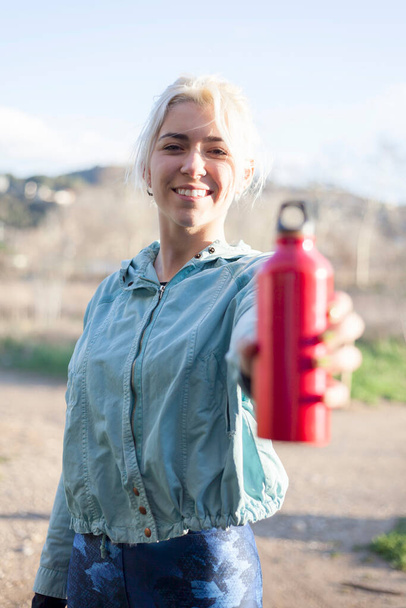 Une femme sportive souriante heureuse passant une bouteille d'eau à la caméra - Photo, image