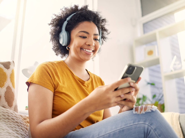 Relax, couch and woman with a cellphone, headphones and happiness with stress relief, audio and streaming music. Happy, female person and girl on a sofa, headset and smartphone with wellness and song. - Foto, Imagem