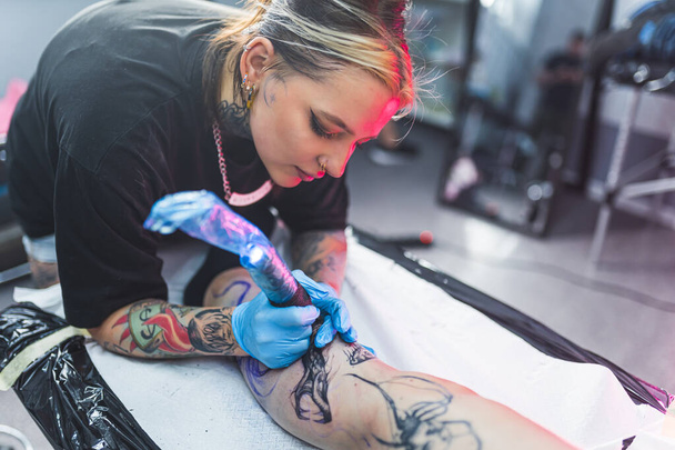 tattooist tattooing womans leg using a machine and with gloves. High quality photo - Fotoğraf, Görsel