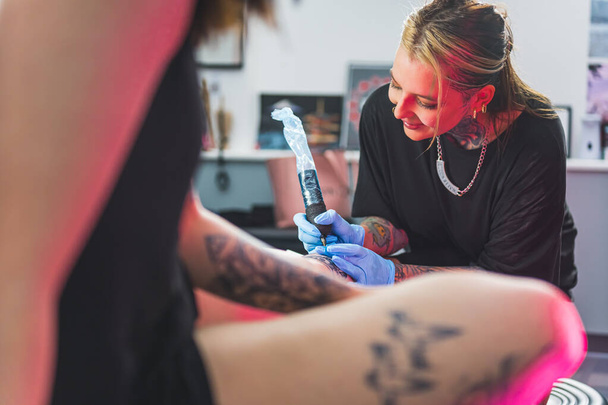 tatuagem artista menina desenho uma nova tatuagem e falando com seu cliente, tiro médio. Foto de alta qualidade - Foto, Imagem