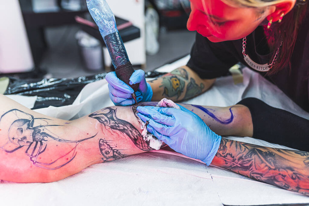 A professional tattoo artist makes a black and white tattoo on a womans leg, applying in ink. The process of tattooing the skin. High quality photo - Foto, imagen
