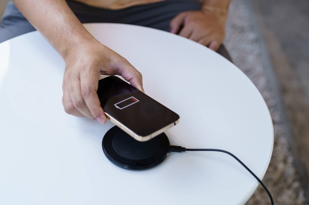 Charging mobile phone battery with wireless charging device in the table. Smartphone charging on a charging pad. Mobile phone near wireless charger Modern lifestyle technology concept - Zdjęcie, obraz