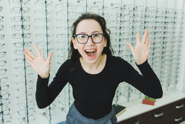 A young woman chooses glasses in an optical store. Stand with glasses. Vision correction. Woman in glasses. Portrait of a woman in corrective glasses. - Photo, Image