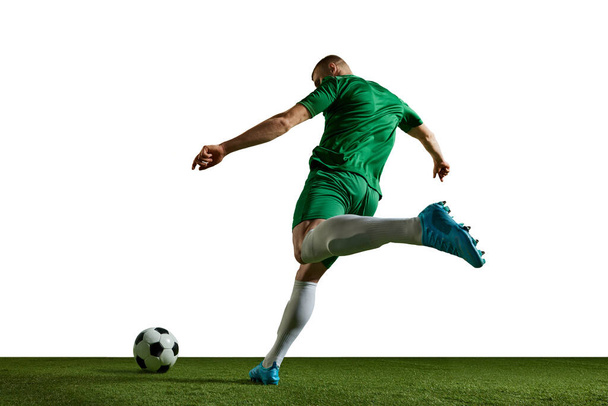 Young man, football player in green uniform in motion, kicking ball, training, playing against white background. Concept of professional sport, action, lifestyle, competition, hobby, training, ad - Foto, afbeelding