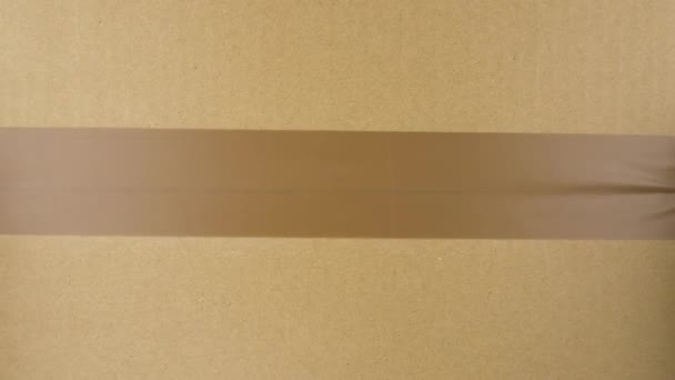 Manos sellando caja de cartón con cinta adhesiva. Vista desde arriba - Metraje, vídeo