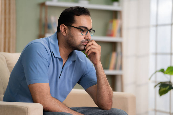 Hombre indio preocupado pensamiento profundo mientras está sentado en el sofá en casa - concepto de problema financiero, ruptura del amor y enfermedad mental - Foto, Imagen