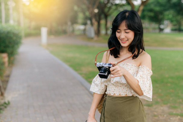 Portrait of young asian woman traveler with weaving hat and basket and a camera on green public park nature background. Journey trip lifestyle, world travel explorer or Asia summer tourism concept. - Foto, imagen