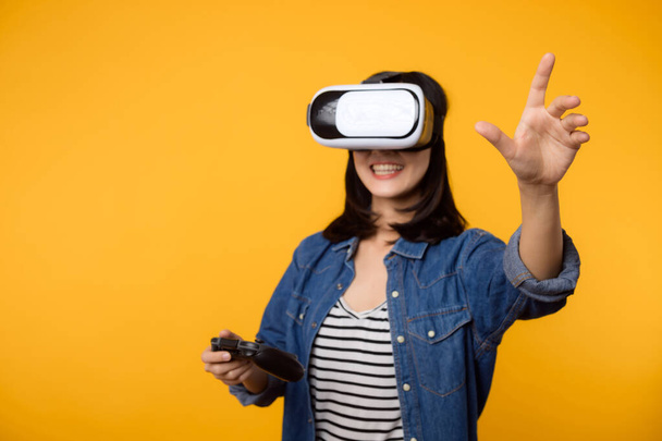 Asiatische junge Frau glücklich Erfolg trägt Virtual-Reality-Headset-Spiel Unterhaltung und hält Steuerknüppel-Controller isoliert auf gelbem Hintergrund. Gewinner des Cyberfuture-Videospielkonzepts. - Foto, Bild