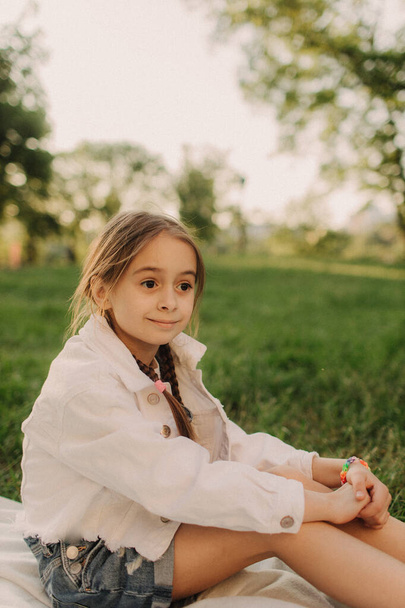 Pieni rento tyttö hengittää raitista ilmaa vihreässä metsässä. Kaunis teini tyttö valkoisissa vaatteissa istuu vihreällä ruoholla puistossa aurinkoisena kesäpäivänä. Viehättävä ukrainalainen lapsi muotokuva.Happy lapsuuden ja ulkoilun käsite - Valokuva, kuva