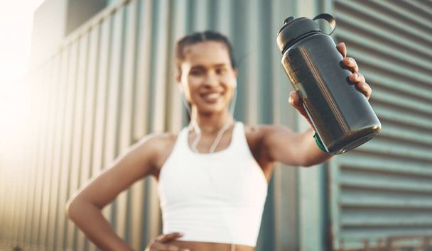 Earphones, runner or happy woman with bottle in city to hydrate or relax on exercise or water break. Tired blur, thirsty or portrait of girl with liquid for hydration in fitness training or workout. - Фото, изображение