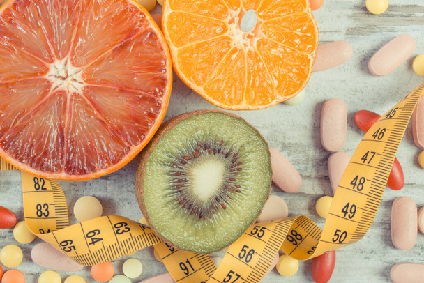 Fresh natural fruits containing vitamins, tape measure and medical pills. Choice between healthy nutrition and supplements - Foto, imagen