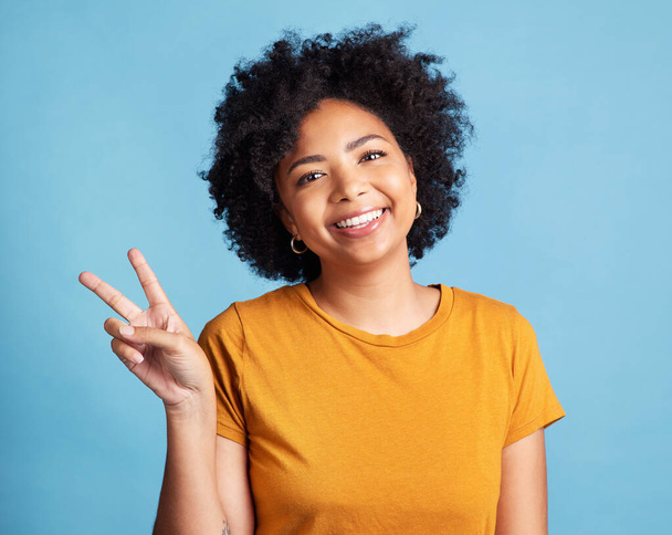 Peace sign, portrait of a woman with smile and against a blue background for satisfaction. Positivity or cheerful, health wellness and face of happy female person pose against studio backdrop. - Photo, Image