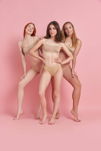 Full-length image of beautiful, slim, fit young women in beige underwear against pink studio background. Concept of natural beauty, body and skin care, health, fitness, wellness, ad - Φωτογραφία, εικόνα