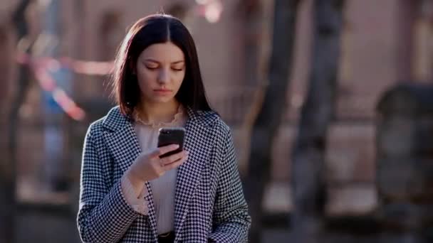 Une jeune fille à l'extérieur est en train de taper un message, à la recherche d'informations sur son téléphone. Images 4k de haute qualité - Séquence, vidéo
