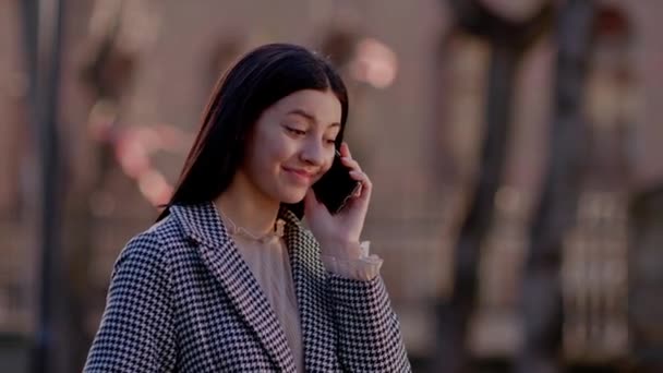 Hymyilevä nuori ruskeaverikkö nainen takissa puhuu puhelimessa. Kiva puhelinkeskustelu. Laadukas 4k kuvamateriaalia - Materiaali, video