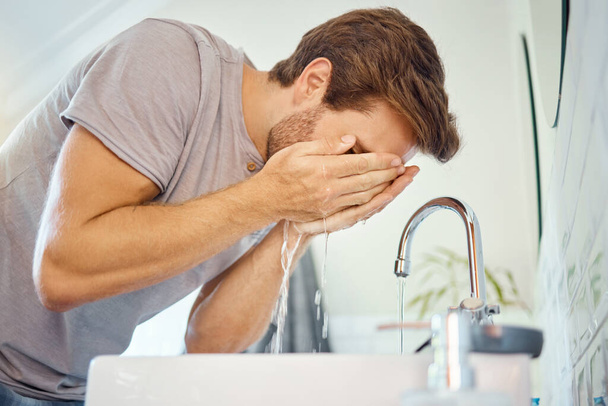 Man, washing and face with water for cleaning at tap in bathroom, morning skincare routine and grooming at home. Young guy, facial and wet splash at faucet, basin and dermatology for personal hygiene. - Photo, image