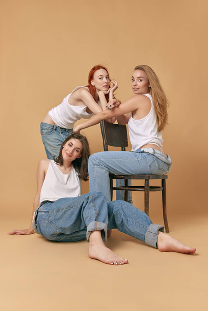 Friends. Portrait of attractive young women with blonde, brown and redhead hair color, posing in jeans and white singlet against studio background. Concept of beauty, body and skin care, health, ad - Foto, Bild