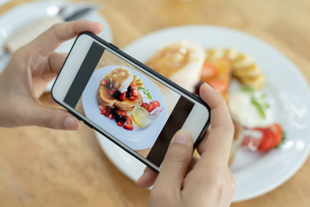 Ravintolan omistaja ottaa kuvan pöydällä olevasta ruoasta älypuhelimella julkaistavaksi verkkosivustolle. Online elintarvikkeiden toimitus, tilauspalvelu, vaikuttaja, arvostelu, sosiaalinen media, osake, markkinointi, kiinnostus. - Valokuva, kuva
