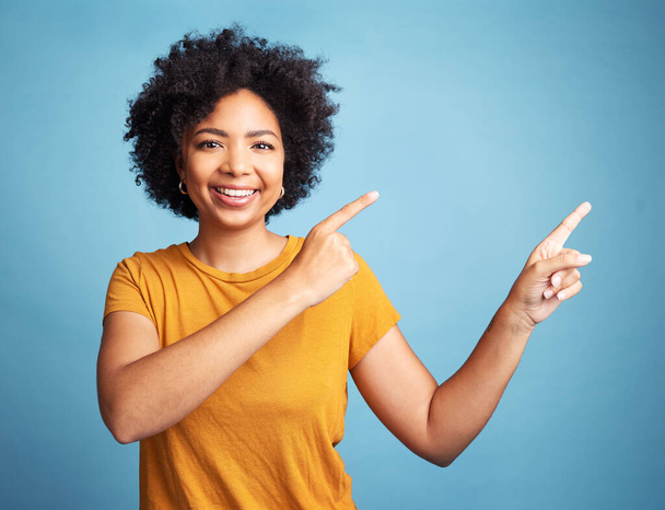 Happy, portrait of woman pointing and against blue background for product placement. Direction or marketing, advertising or giveaway and female person pose with hand gesture in studio backdrop. - Valokuva, kuva