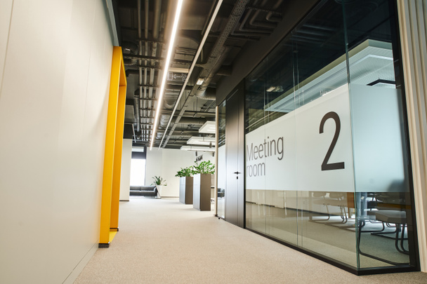 długi i szeroki korytarz z oświetleniem LED, zielone rośliny, sala konferencyjna za szklaną przezroczystą ścianą w nowoczesnym środowisku współpracowników z nowoczesnym wnętrzem, koncepcja organizacji miejsca pracy - Zdjęcie, obraz