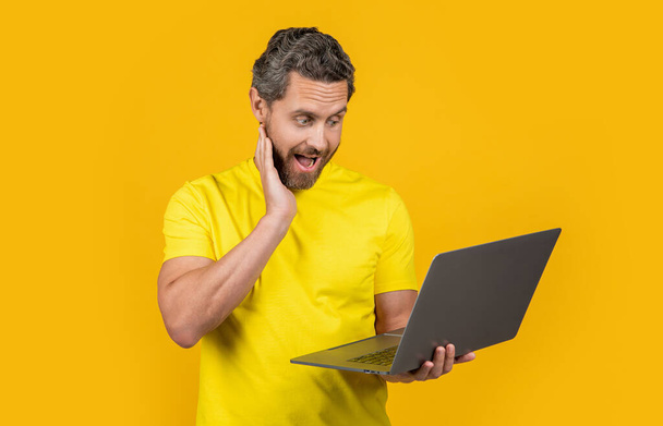 image of surprised man programmer with laptop. man programmer isolated on yellow. man programmer on background. man programmer in studio. - Photo, image