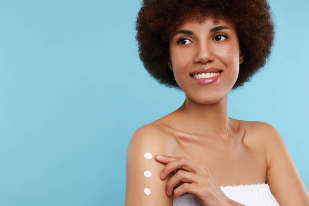 Beautiful young woman applying body cream onto arm on light blue background, space for text - Foto, afbeelding