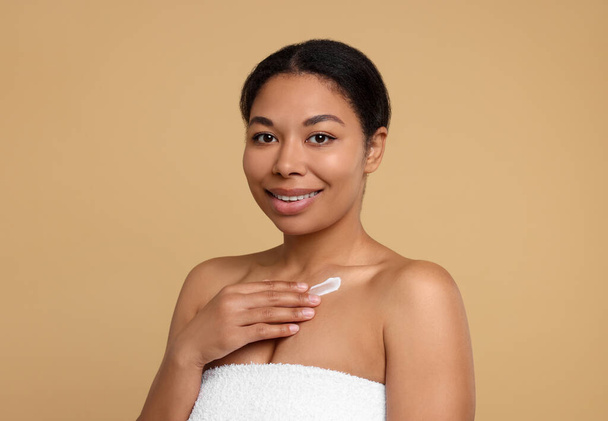 Young woman applying cream onto body on beige background - Foto, afbeelding