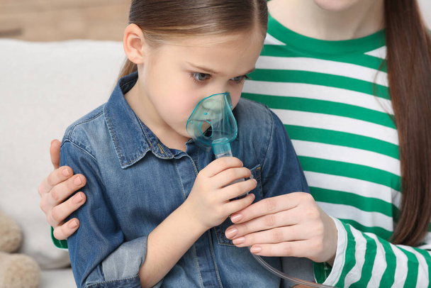 Mother helping her sick daughter with nebulizer inhalation at home - Foto, imagen