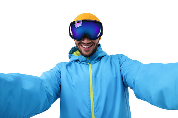 Joven sonriente con gafas de esquí tomando selfie sobre fondo blanco - Foto, imagen