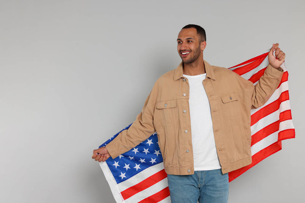 4 lipca - Dzień Niepodległości USA. Szczęśliwy człowiek z amerykańską flagą na jasnoszarym tle, miejsce na tekst - Zdjęcie, obraz