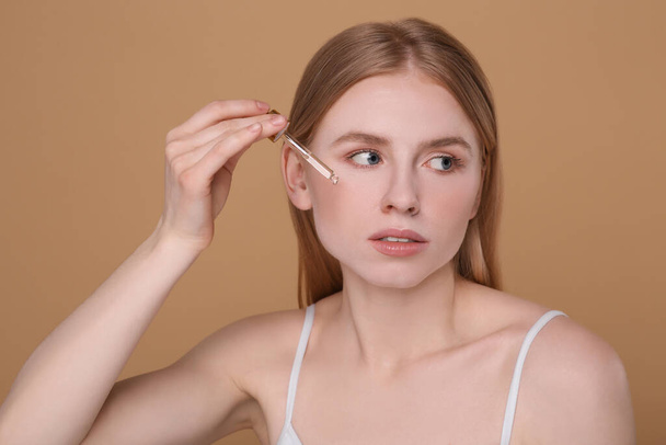 Woman applying essential oil onto face on light brown background - Fotografie, Obrázek